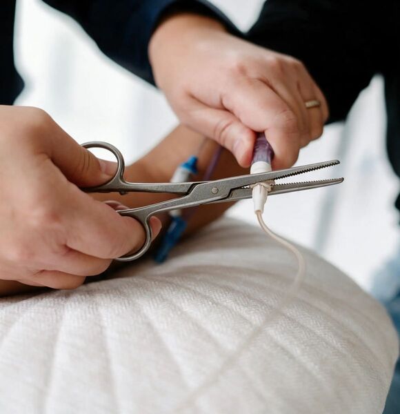 A nurse's hands clamping a metal hemostat onto an IV connector to force it apart