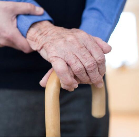 An older person’s hands resting on a walking cane